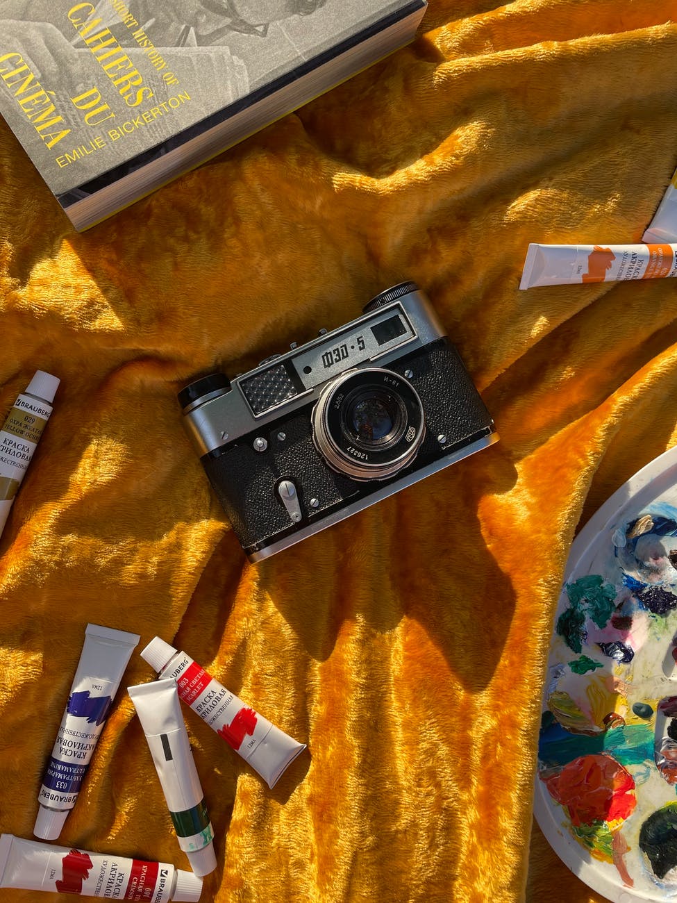 close up shot of an analog camera on a gold textile with paints - items for a creative hobby